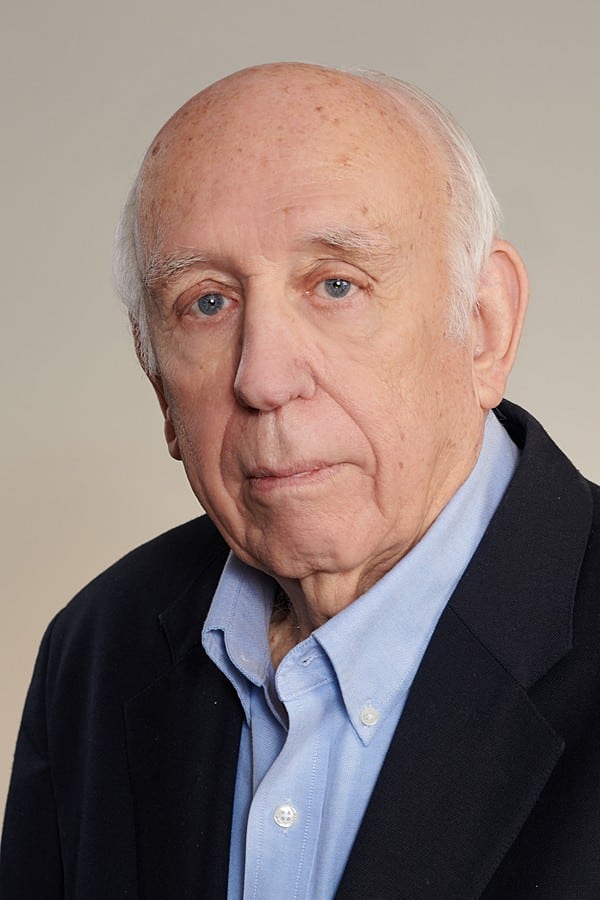 Photo of Dennis Jones, an older man with short white hair on the sides, with balding on top of his head, wearing a black suit jacket and blue dress shirt. 
